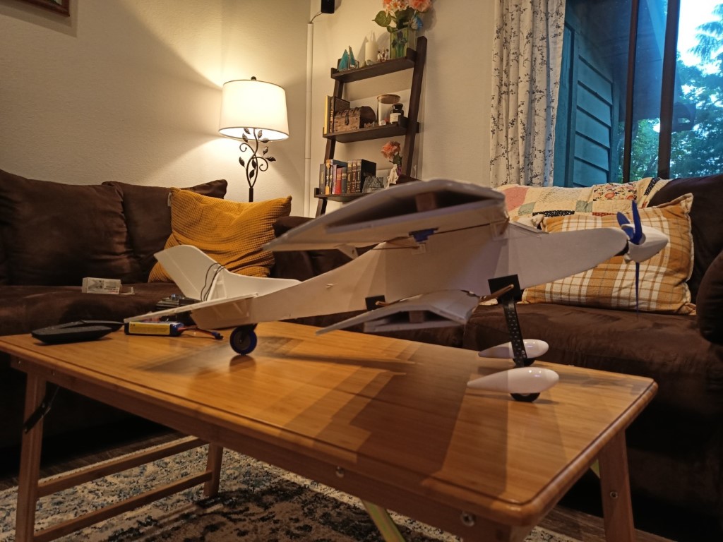 White model seaplane with a blue propeller and pontoons on a coffee table beside a remote and battery