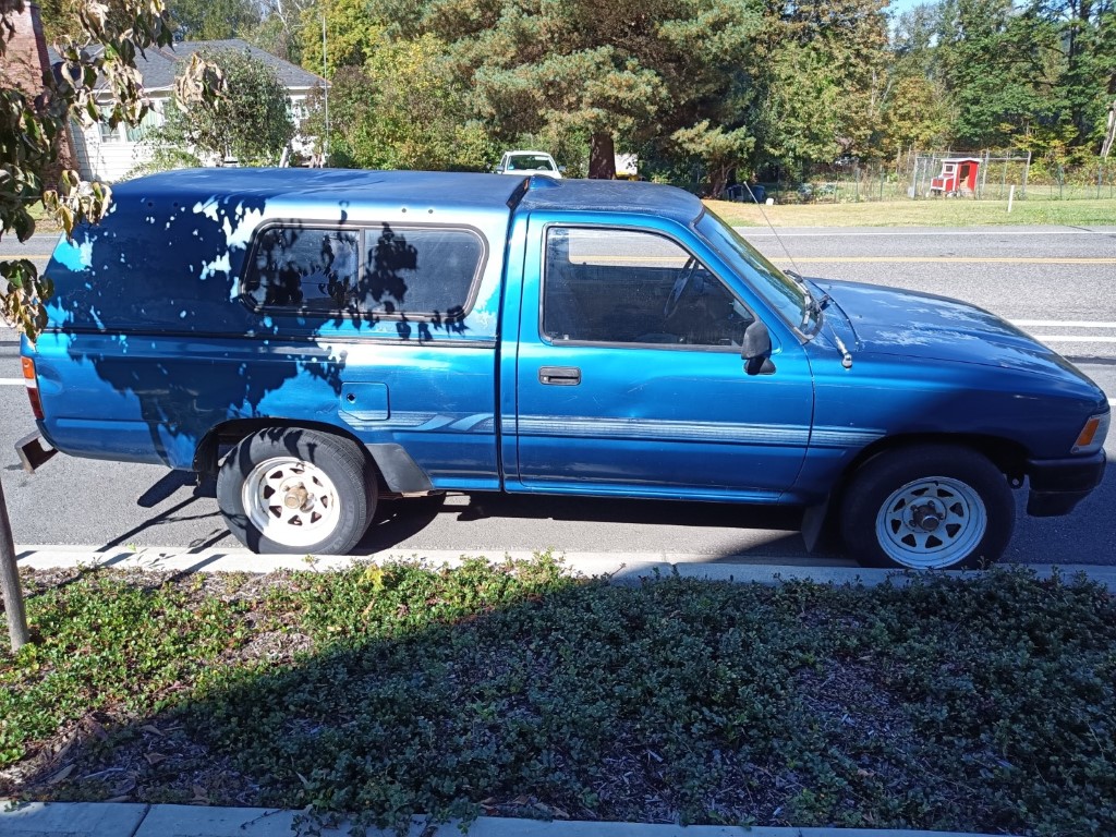 Vintage blue Toyota pickup with a matching camper shell parked on a residential street