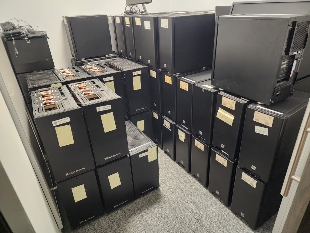 Room of stacked Puget Systems towers with side panels open showing heat pipes, marked with yellow sticky notes