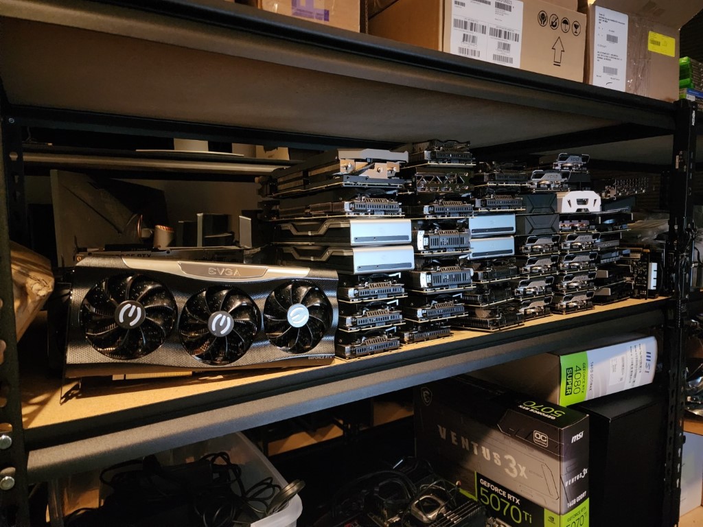 Shelving unit with a triple-fan EVGA card lying flat, a tall stack of vertical GPUs, and MSI retail boxes below
