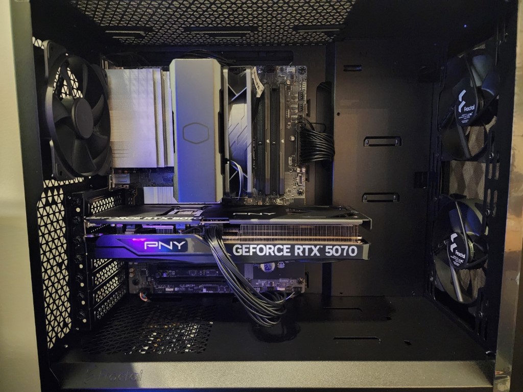 Interior of a black case with a PNY RTX 5070 under purple lighting, a silver tower cooler, and silver RAM