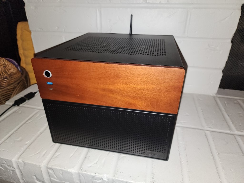 Custom NAS in a compact black case with a wood-grain front panel on a white brick ledge
